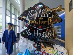A balloon that says \"the tassel was worth the hassle\" and a graduate in blue robes walking by